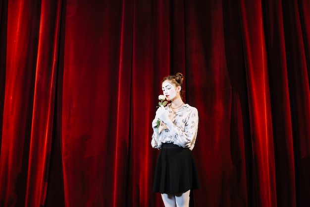 Femme mime debout devant un rideau rouge sentant la rose blanche