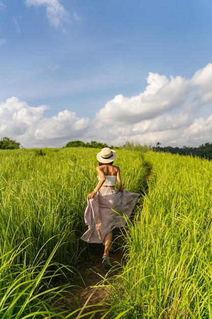 Une femme mince au chapeau voyage dans un pays exotique et marche parmi les champs verts de la campagne