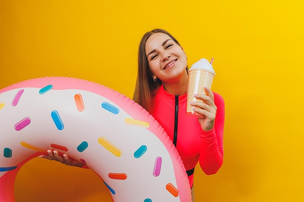 Une femme mince dans un maillot de bain rose vif sur fond jaune Elle tient un beignet de piscine gonflable Beach fashion