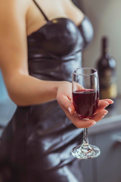 femme mince dans une robe en cuir tient un verre à vin avec du vin rouge