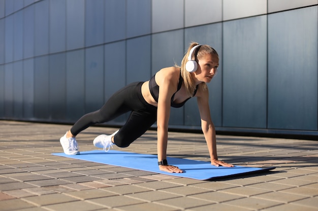 Femme mince déterminée athlétique faisant des exercices sur le tapis bleu en plein air.