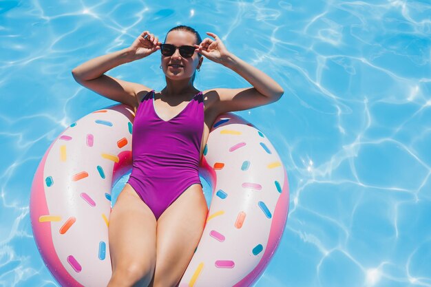 Femme mince à lunettes de soleil dans la piscine dans un anneau de natation gonflable dans un maillot de bain lumineux photo d'été photographie de natation photos de femme d'été mode de plage