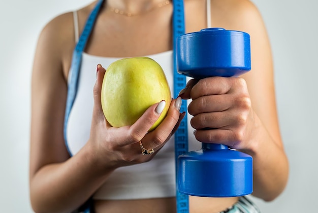 Femme mince méconnaissable avec ruban à mesurer tenant des haltères bleus et pomme