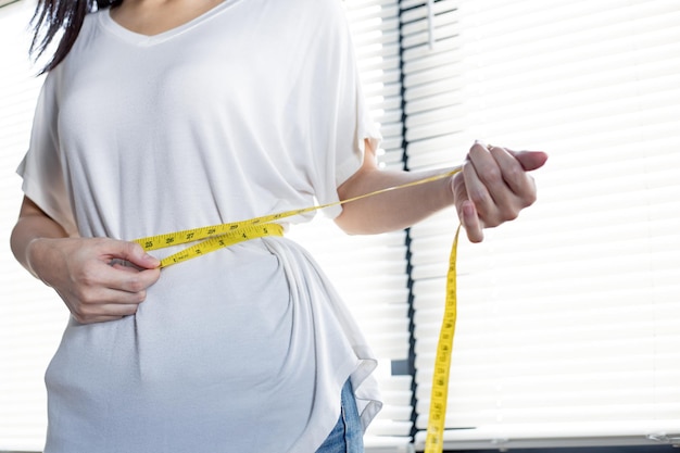 Femme mince mesurant sa taille par ruban à mesurer après régime. Fille avec centimètre. Jeune femme avec une taille parfaite avec un ruban à mesurer. Mains mesurant avec du ruban adhésif au niveau de l'abdomen.