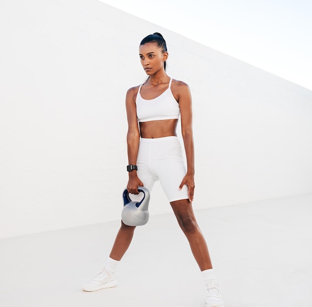 Femme mince en vêtements de fitness blancs faisant de l'exercice avec kettlebell à l'extérieur