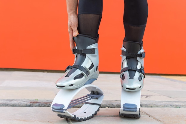 Une femme a mis des bottes de saut kangoo grises avant l'entraînement de remise en forme sur fond de couleur orange