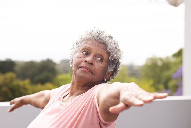 Une femme mixte âgée aux cheveux gris bouclés pratique le yoga à l'extérieur.