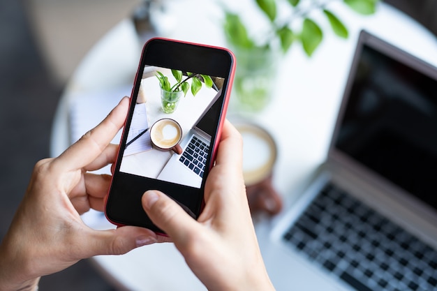 Femme Mobile Prenant Une Photo De Cappuccino Dans Une Tasse Et Un Clavier D'ordinateur Portable Sur La Table Tout En Vous Relaxant Dans Un Café