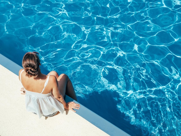 Femme à la mode assise au bord de la piscine sur le pont vide