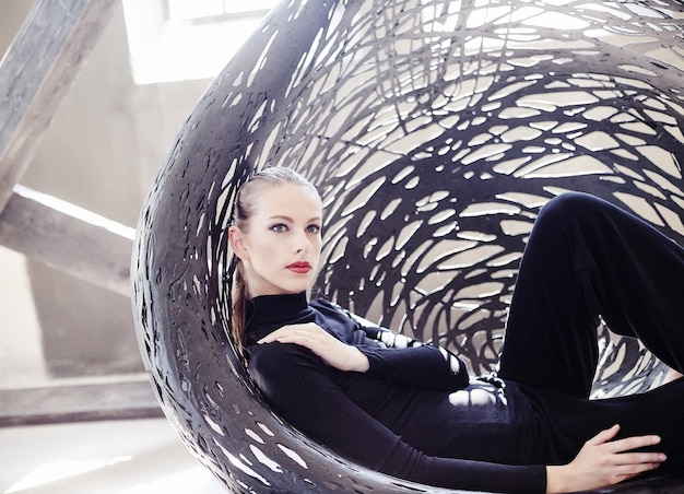 Femme à la mode dans un vêtement noir allongé sur une chaise ronde.