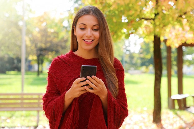 Femme de mode discutant en ligne avec un téléphone intelligent dans le parc de la ville.