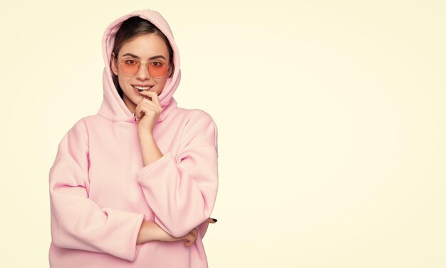 Femme à la mode heureuse souriante gardant le doigt sur la lèvre dans un hoodie rose décontracté isolé sur blanc