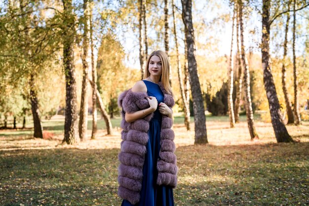 Femme de mode. Jeune fille souriante en manteau de fourrure posin en automne parc avec arbres et lierre