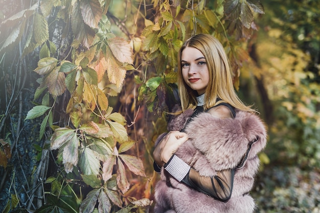 Femme de mode. Jeune fille souriante en manteau de fourrure posin en automne parc avec arbres et lierre