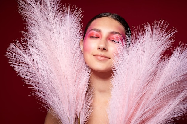 Femme à la mode avec un maquillage lumineux de peigne posant des plumes pelucheuses fond rose inchangé