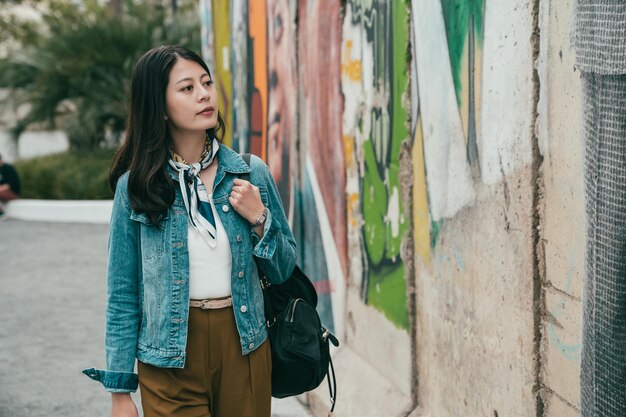 femme de mode marchant dans la rue et regardant les graffitis sur le mur en rentrant chez elle