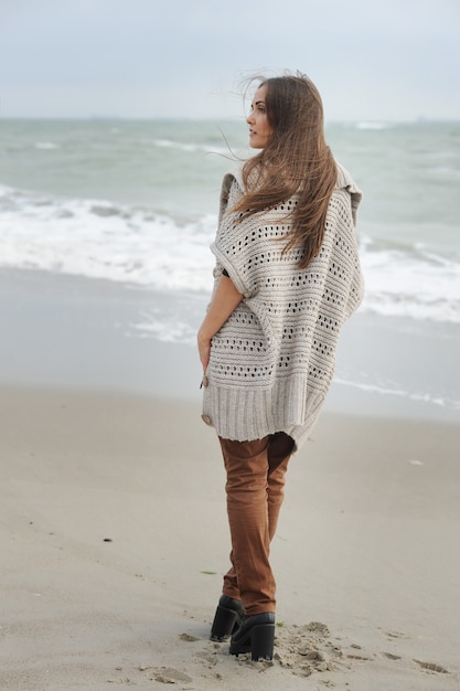 Femme de mode marchant seule sur une plage de la mer, tissu oversize décontracté, automne en plein air