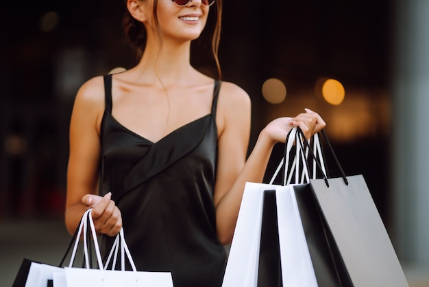 Femme à la mode vêtue d'une robe noire avec des sacs à provisions.