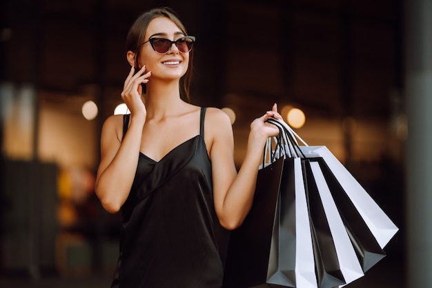 Femme à la mode vêtue d'une robe noire avec des sacs à provisions.