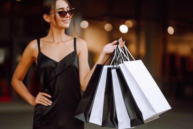 Femme à la mode vêtue d'une robe noire avec des sacs à provisions.