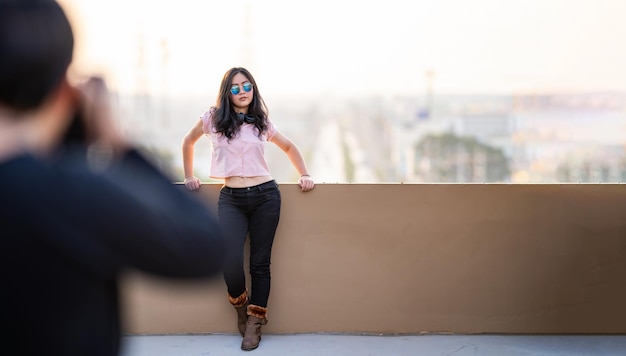 Une femme modèle asiatique pose pour un photographe pour photographier un endroit sur le toit avec une vue floue sur la ville au crépuscule