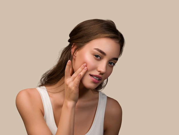 Femme modèle de beauté avec un maquillage naturel sain et une peau propre touchant son visage Fond de couleur marron