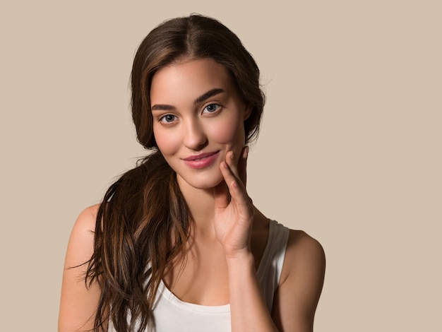 Femme modèle de beauté avec une peau propre et naturelle en bonne santé touchant son visage Fond de couleur marron