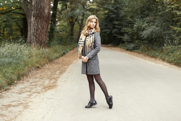 Femme modèle chaud en écharpe chaude vintage dans un manteau et des chaussures marchant sur la route dans le parc.