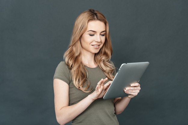 Femme moderne. Belle jeune femme aux cheveux blonds souriant et utilisant une tablette numérique