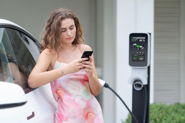 Femme moderne et respectueuse de l'environnement rechargeant un véhicule électrique à partir d'une station de recharge EV à domicile Utilisation innovante de la technologie EV pour suivre la consommation d'énergie afin d'optimiser la charge de la batterie à la maison Synchronos