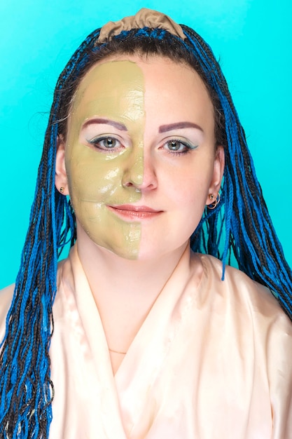 Une femme avec la moitié de son visage dans un masque d'argile verte sur une surface bleue