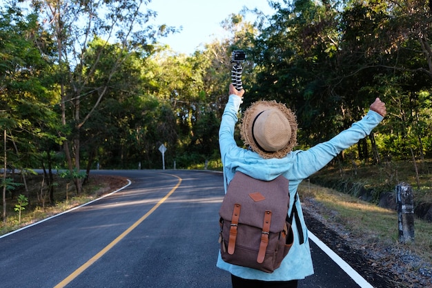 Photo une femme avec un monopode marchant sur la route au milieu des arbres