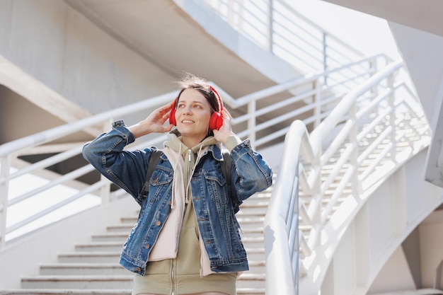 Une femme monte les marches et écoute de la musique ou un podcast avec un gros plan de portrait de casque rouge