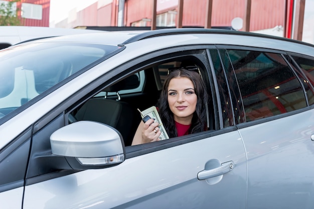 Femme montrant des billets en dollars depuis la fenêtre de la voiture