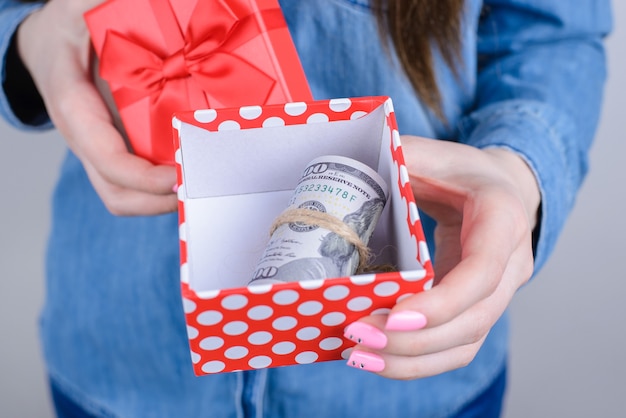 Femme montrant une boîte cadeau ouverte avec un paquet d'argent isolé