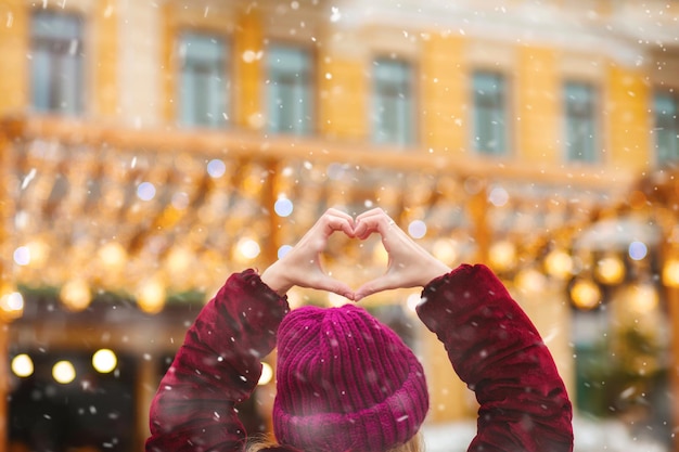 Femme montrant la forme de coeur de ses doigts sur un fond de lumières bokeh