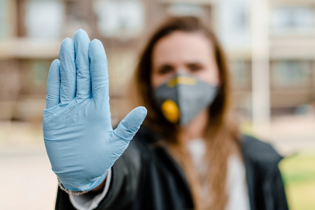 Femme montrant le panneau d'arrêt avec la main portant un masque respiratoire et des gants à l'extérieur sur la rue de la ville