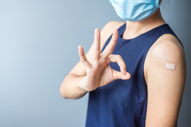 femme montrant un signe OK avec un bandage après avoir reçu le vaccin covid 19
