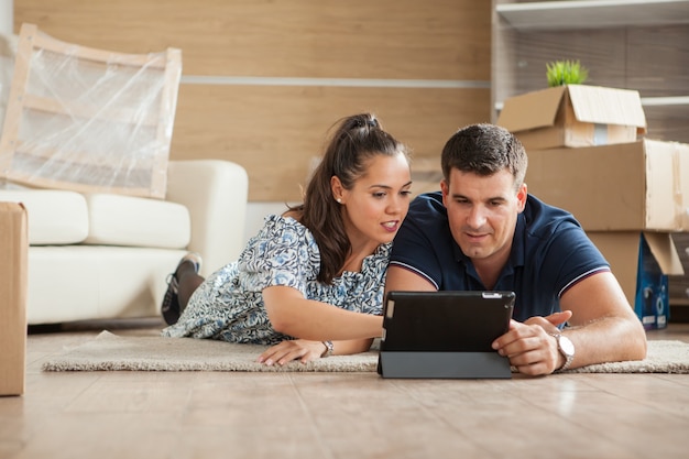 Femme montrant à son mari le lit de leur nouvel appartement sur leur tablette