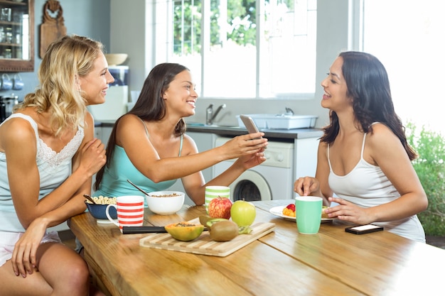 Femme montrant un téléphone portable à un ami à la table du petit déjeuner