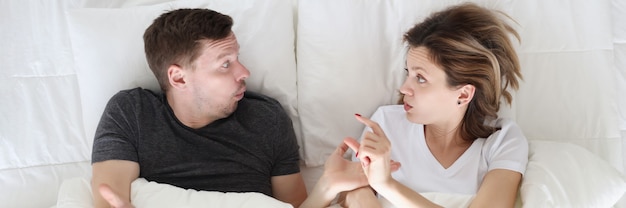 Une femme montre à un homme un geste de taille avec ses doigts en position couchée avec lui dans son lit, taille de dignité masculine