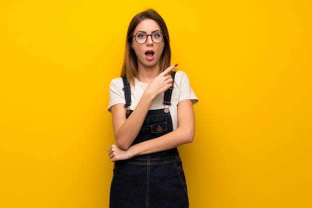 Femme sur un mur jaune surpris et pointant le côté