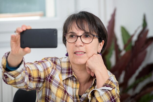 Femme mûre avec une chemise à carreaux faisant selfie