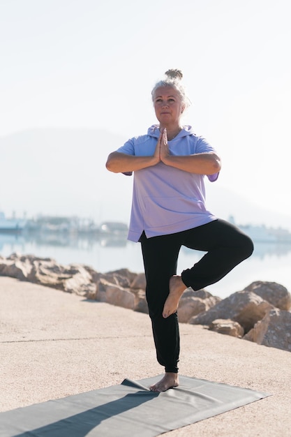Femme mûre avec des dreadlocks travaillant à faire des exercices de yoga sur la plage de la mer bien-être bien-être et concept d'âge actif des personnes âgées