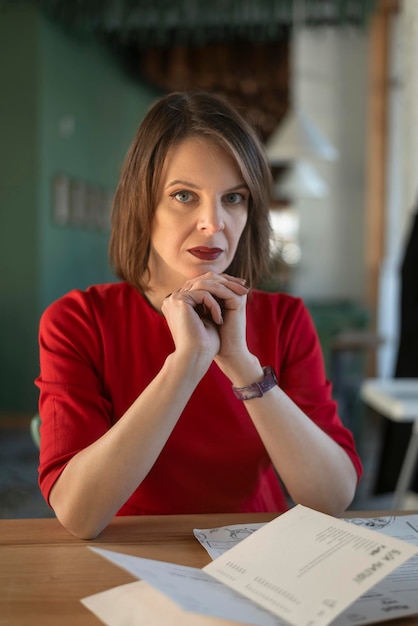 Femme mûre élégante en blouse rouge est assis à table dans le café Portrait de femme d'affaires à la cafétéria Cadre vertical