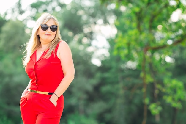 Femme mûre élégante dans des lunettes de soleil sur le fond des arbres verts