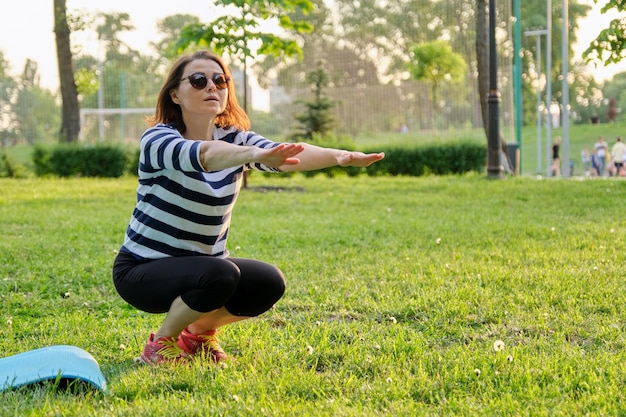 Femme mûre faisant des exercices de remise en forme sur tapis dans le parc. Sports actifs mode de vie sain des personnes d'âge moyen, corps et beauté