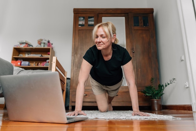 Femme mûre à la maison faisant du yoga sportif sur le sol avec des cours en ligne pour ordinateur portable