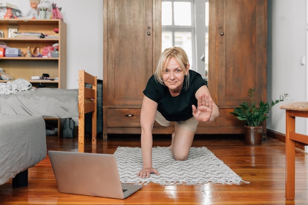 Femme mûre à la maison faisant du yoga sportif sur le sol avec des cours en ligne pour ordinateur portable