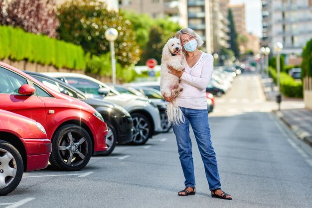 Femme mûre marchant avec un chien dehors un masque d'antivirus